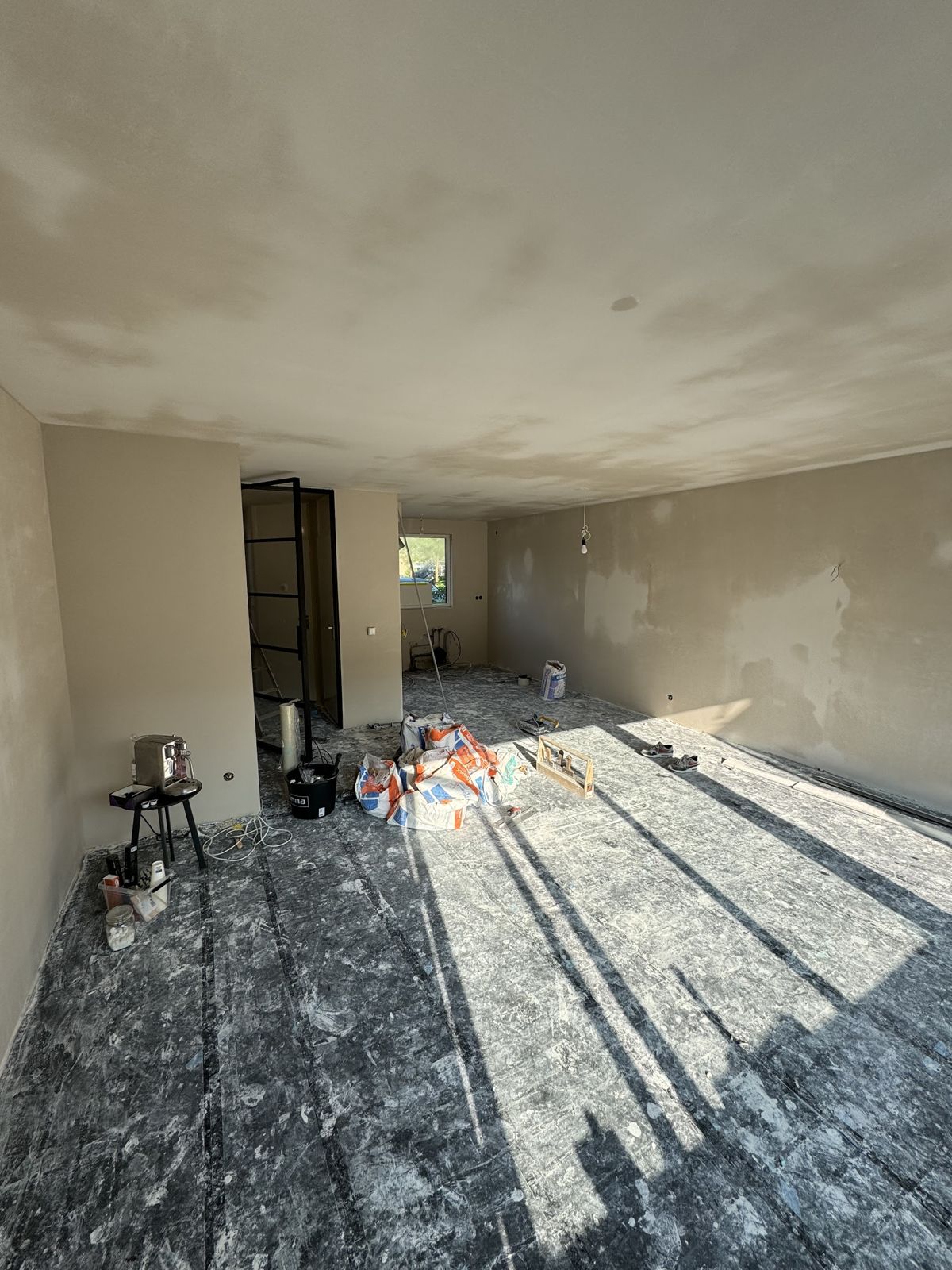 Lege woonkamer met pas gestucte wanden en plafond, vloer afgedekt