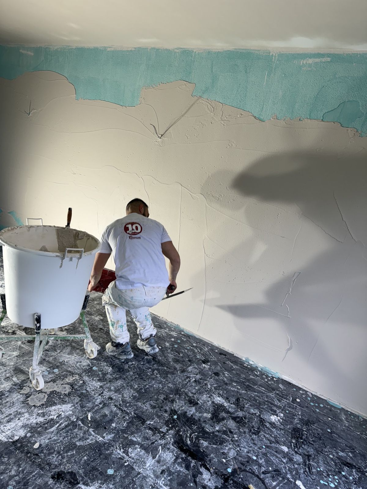 Stukadoor zet een wand op over turquoise voorstrijk, speciekuip op standaard