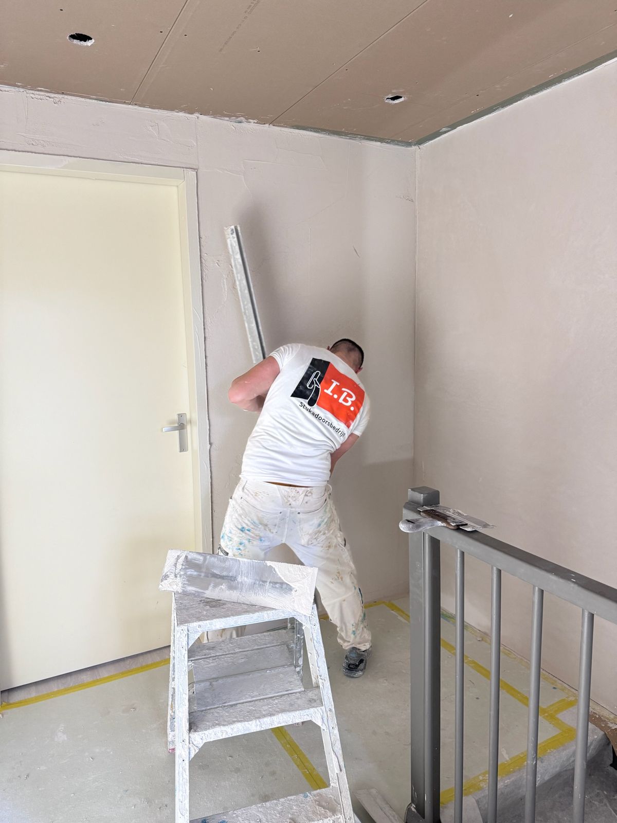 Stukadoor in een I.B.-shirt aan het werk in een trapgat bij de overloop
