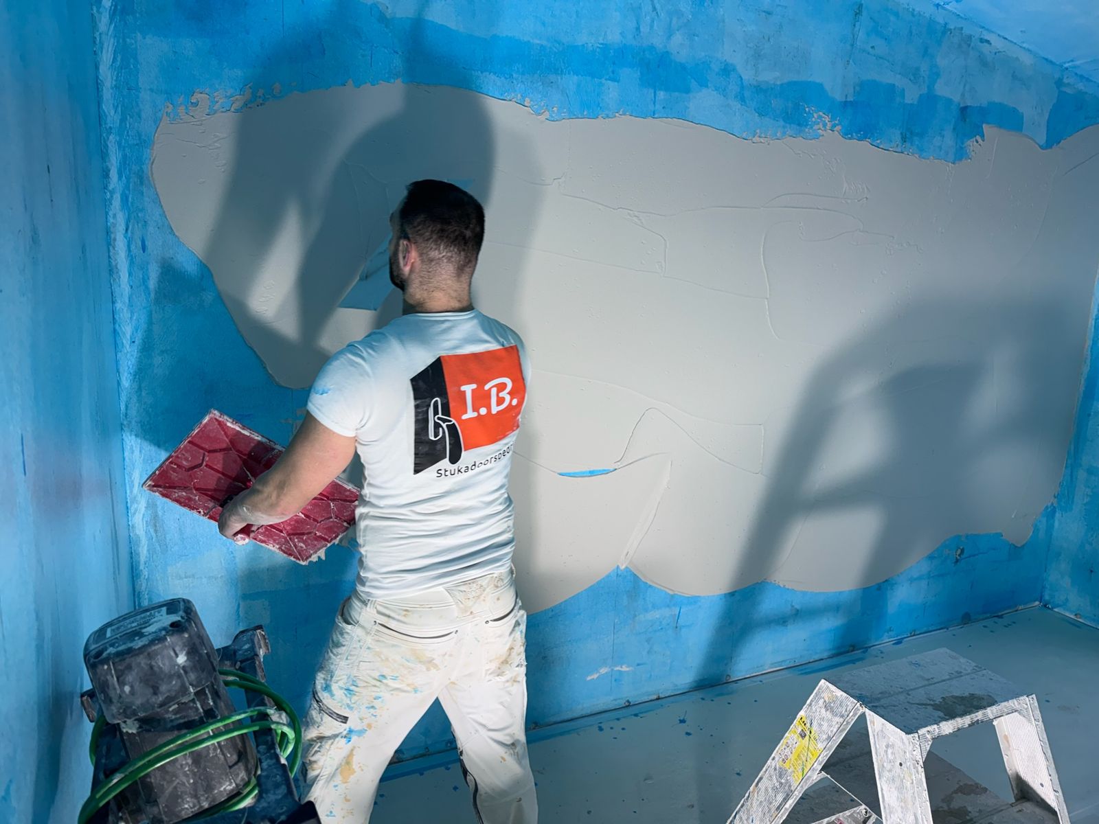 Stukadoor in het I.B.-shirt zet een wand op over blauwe voorstrijk