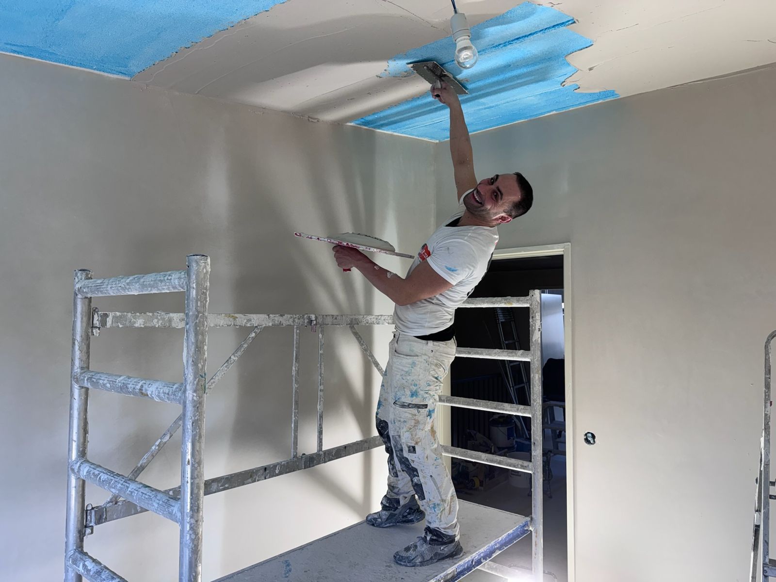 Stukadoor op een rolsteiger stuct een plafond over blauwe voorstrijk